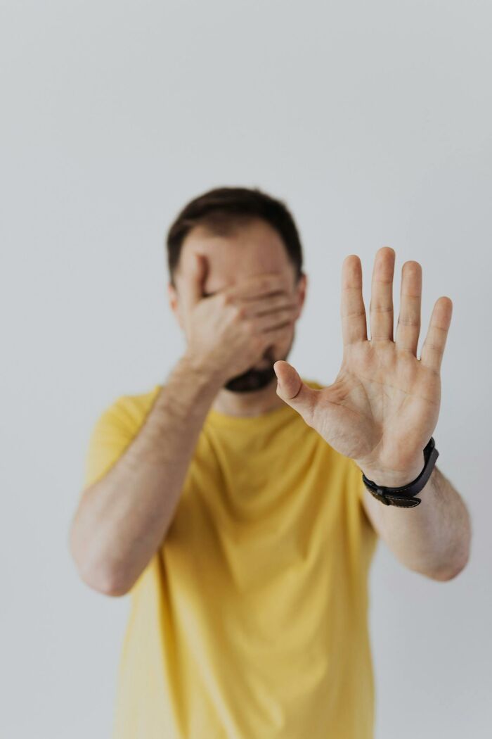 Man in yellow shirt covering face with one hand and raising the other, depicting bizarre moments that challenge sanity.