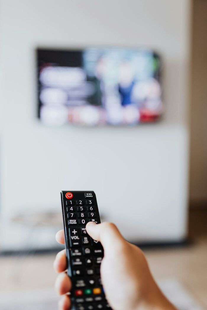 Hand holding a TV remote control in front of a blurred screen, illustrating childhood habits and habits realization.