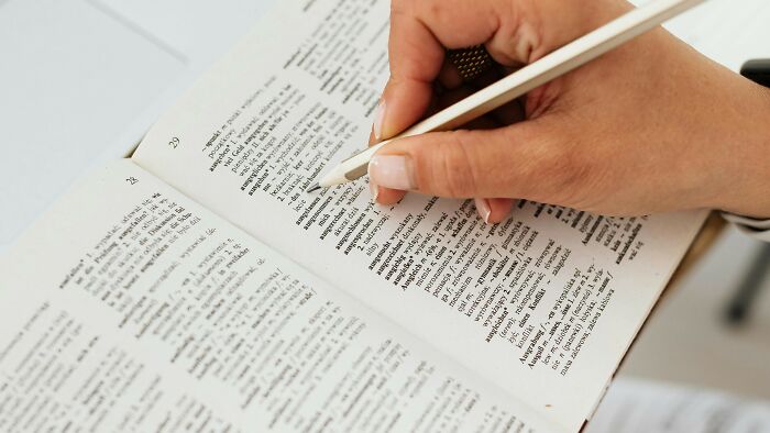 Hand holding pencil pointing to SAT-level words in an open dictionary, demonstrating advanced vocabulary skills. Hand holding pencil pointing to SAT-level words in an open dictionary, demonstrating advanced vocabulary skills.