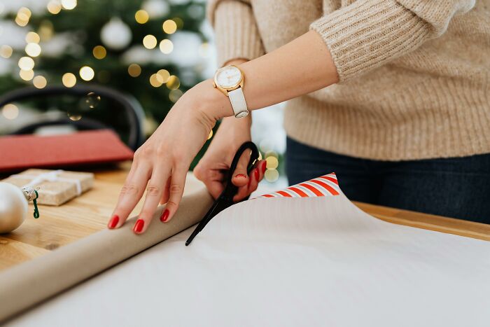 Person cutting wrapping paper with scissors, illustrating relatable and ridiculous everyday moments we’re all guilty of.