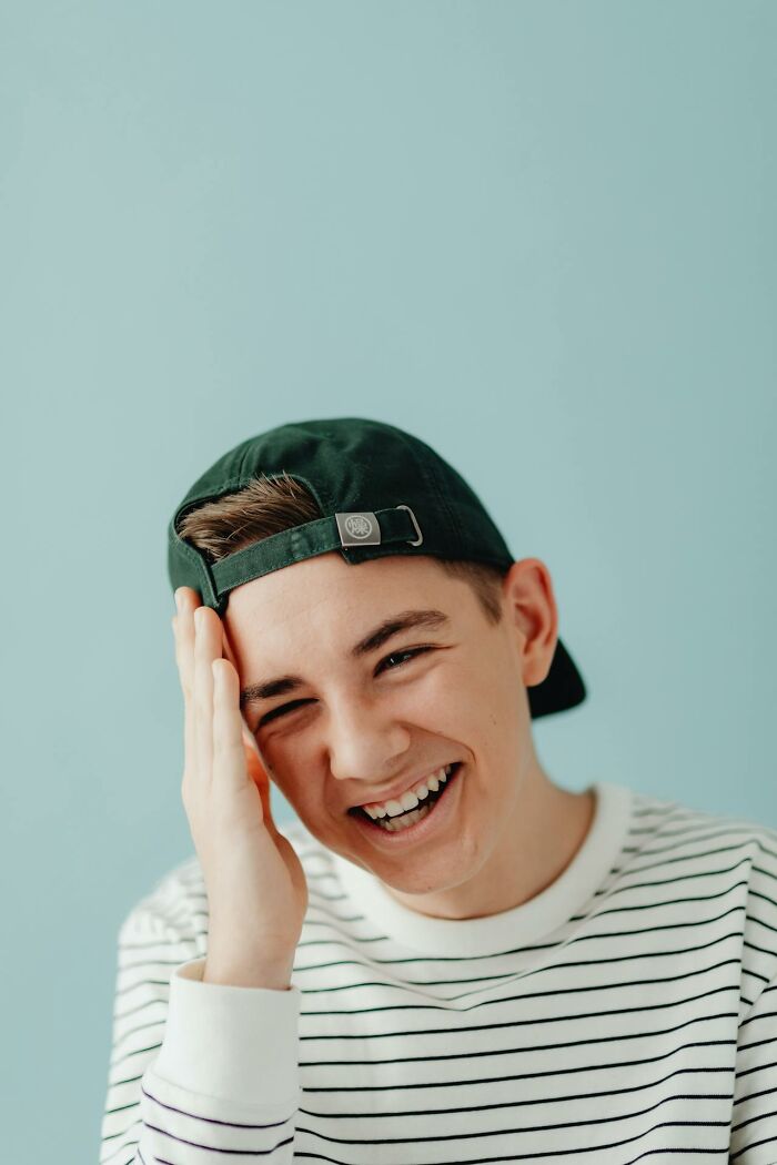 Teenage boy wearing a cap backwards laughing with hand on face, capturing funny and serious moments raising monsters.