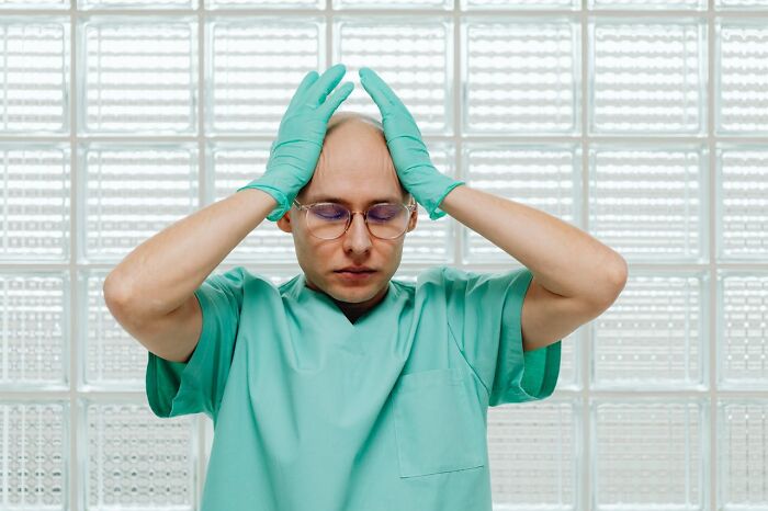 Dentist wearing scrubs and gloves holding head in frustration reflecting on wildest patient horror stories.