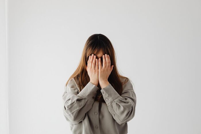 Woman covering her face with hands, expressing deep emotion in a minimalistic setting, relating to dying experiences shared by people.
