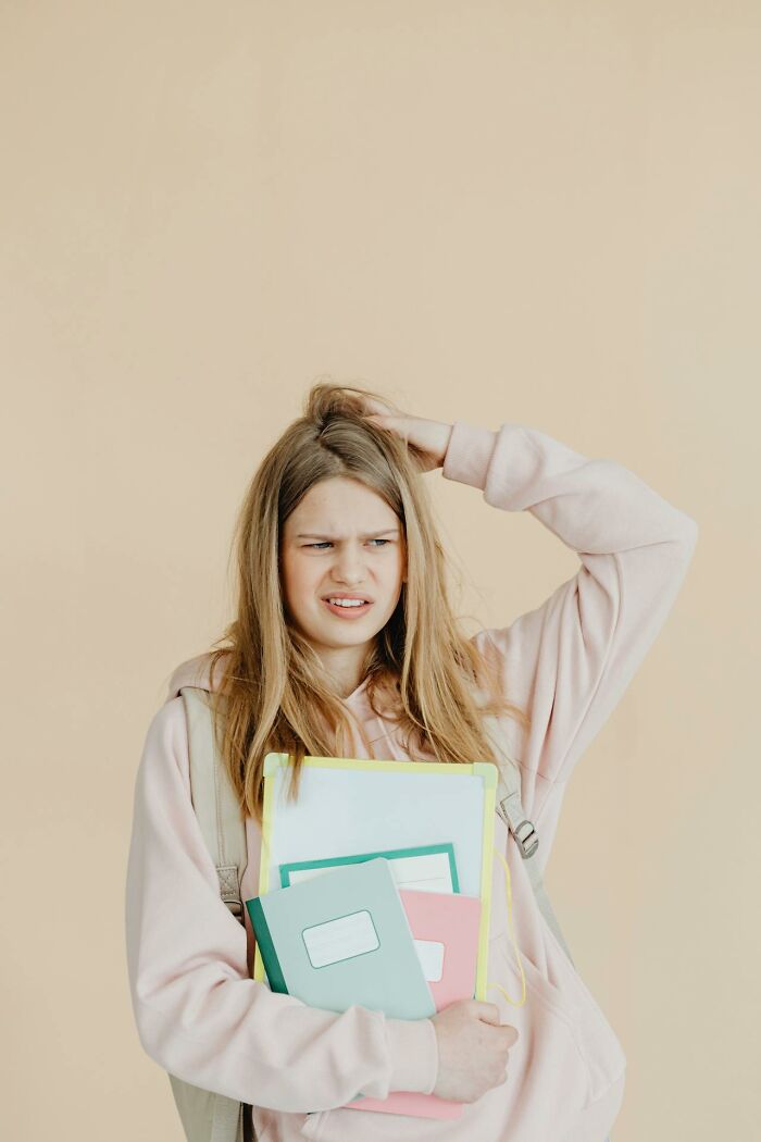 Teen girl looking confused and holding notebooks, capturing bizarre moments that make people question sanity.