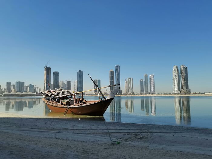 Traditional wooden boat on calm water with a modern city skyline in the background for a cities quiz challenge Traditional wooden boat on calm water with a modern city skyline in the background for a cities quiz challenge