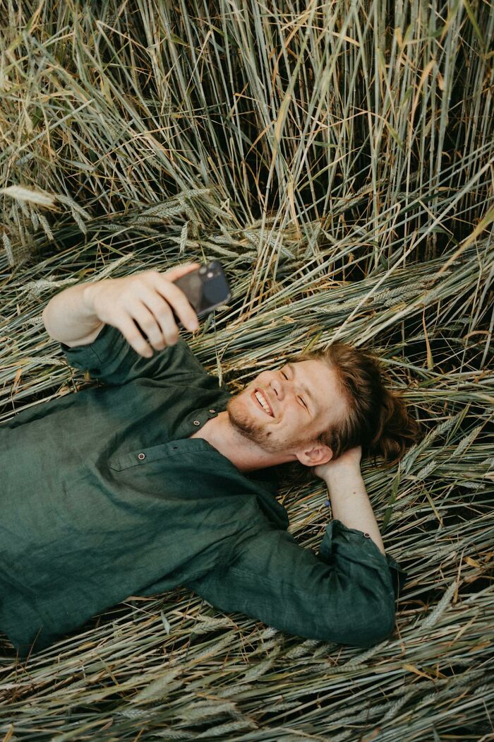 Young man lying in a field of wheat, smiling and taking a selfie, illustrating experiences of people who came back to life.