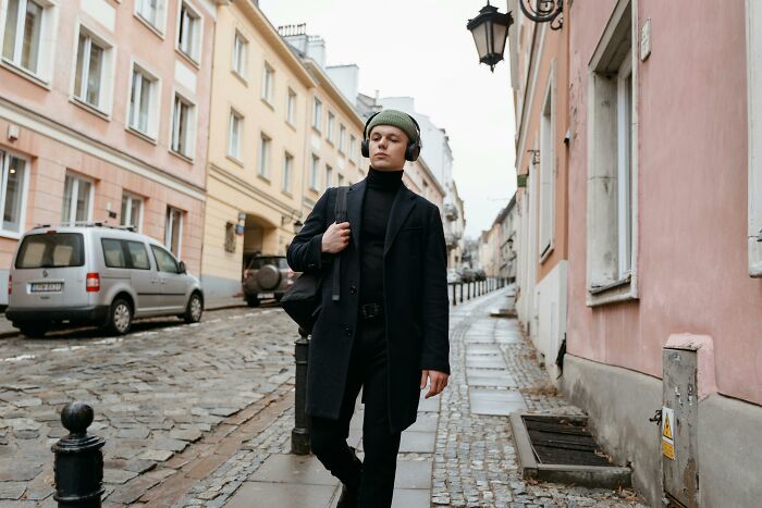 Young person walking on a cobblestone street listening to music, relatable moments capturing ridiculous everyday behaviors.