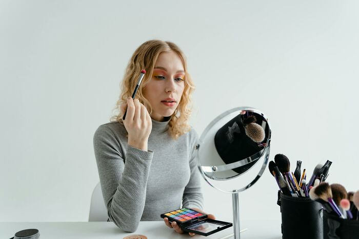 Young woman applying makeup at a table, illustrating stories of folks realizing compulsory things in life were optional.