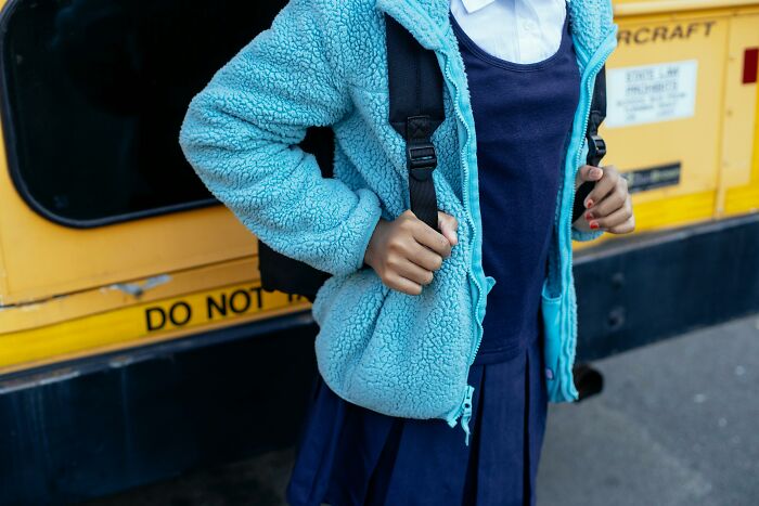 Student in a blue jacket and school uniform standing near yellow bus, illustrating real-life horror story scenarios.