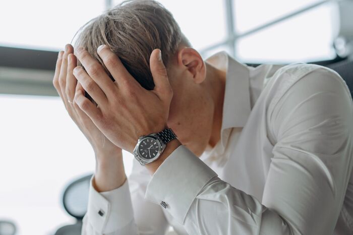 Man in white shirt holding head in hands, experiencing bizarre moment, appearing stressed and overwhelmed indoors.