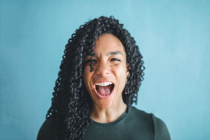 Young woman with curly hair laughing openly against a blue background, expressing childhood habits were anything but normal.