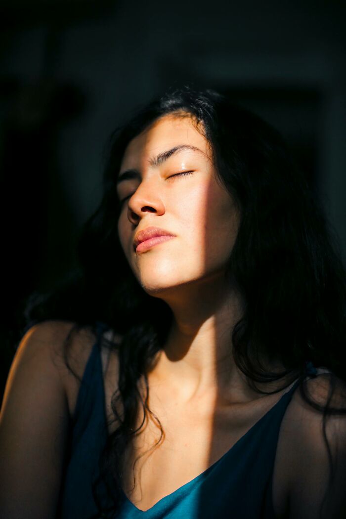 Young woman with closed eyes illuminated by sunlight, reflecting on what dying actually feels like after coming back to life.