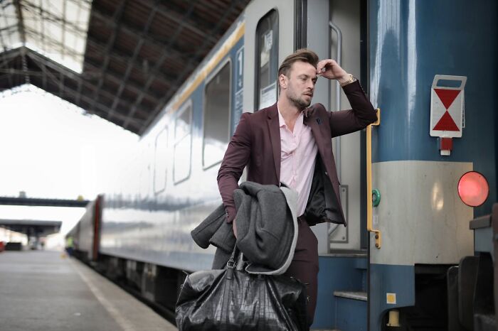 Man in a maroon suit carrying bags and looking stressed while standing next to a train at a station, Karen examples concept. Man in a maroon suit carrying bags and looking stressed while standing next to a train at a station, Karen examples concept.