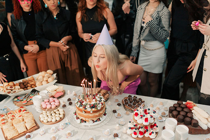 Woman in a party hat blowing out candles on a cake while guests watch, highlighting rich man refuses to pay dispute. Woman in a party hat blowing out candles on a cake while guests watch, highlighting rich man refuses to pay dispute.