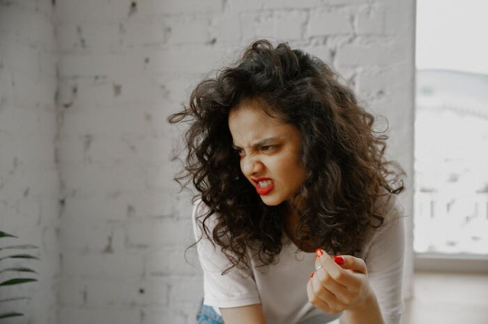 Young woman with curly hair making a bizarre angry face indoors, reflecting moments that made people wonder if they were sane
