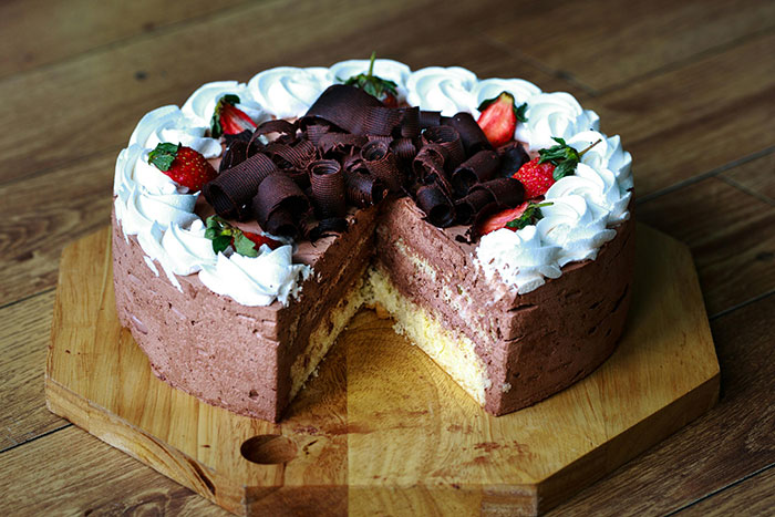 Chocolate and vanilla layered cake with whipped cream, strawberries, and chocolate curls on a wooden cutting board