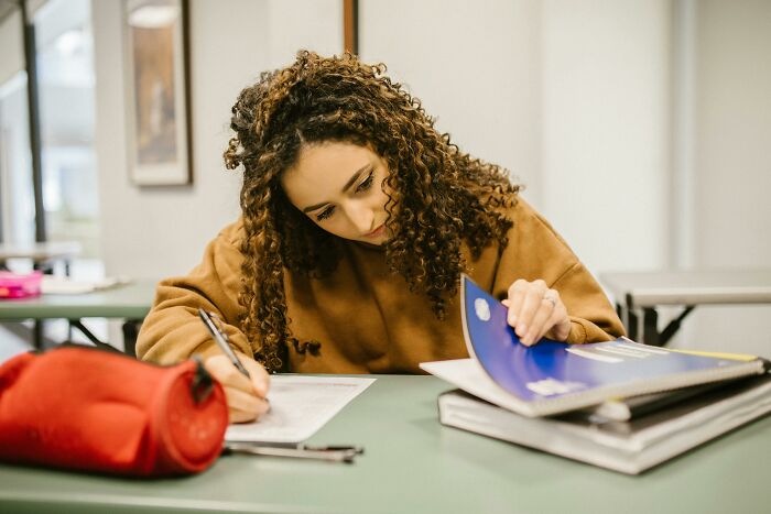 Student with curly hair focused on test papers and notebooks, practicing to test IQ against the average U.S. student.