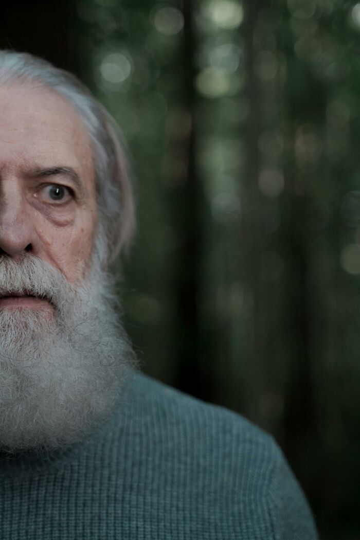 Elderly man with white beard looking cautiously in a forest, evoking bizarre and creepy things witnessed by park rangers and hikers