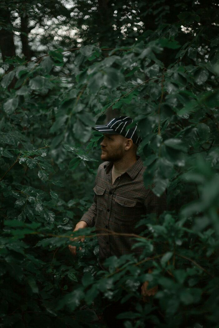 Man in striped cap and plaid shirt navigating dense forest foliage, capturing creepy moments witnessed by park rangers and hikers.