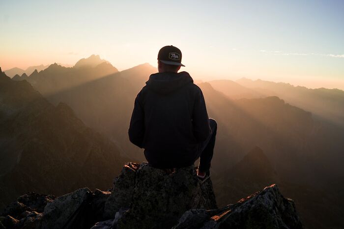 Person seated on rocky mountain peak at sunset, capturing the eerie and bizarre moments witnessed by park rangers and hikers.