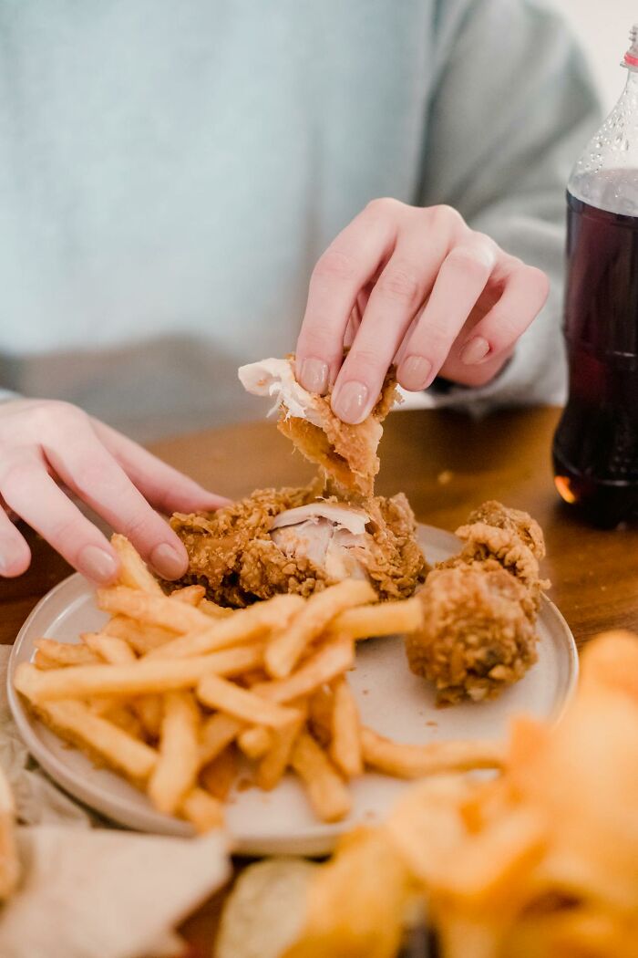 Person tearing fried chicken while eating childhood habits and normal habits contrasted with fries and soda nearby on table.
