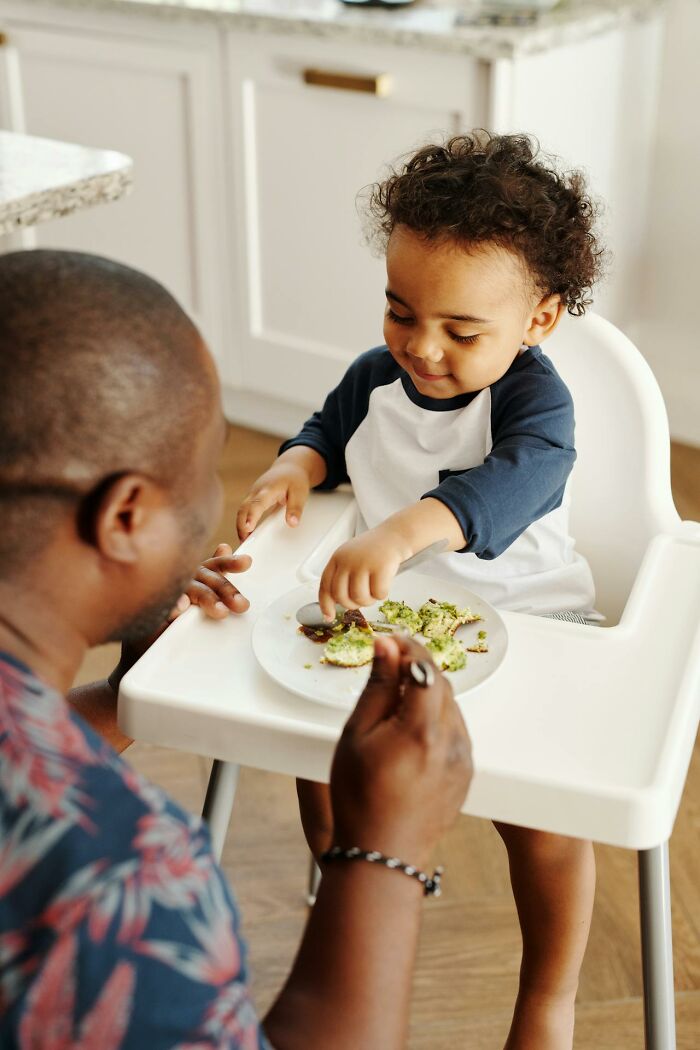 Toddler mischievously playing with food in high chair while parent watches during funny and serious moments raising monsters.