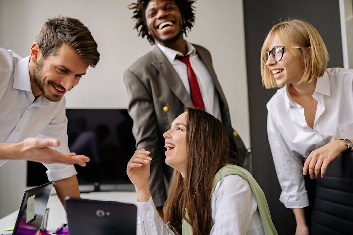 A group of young professionals sharing bizarre moments and laughing together in a modern office setting.