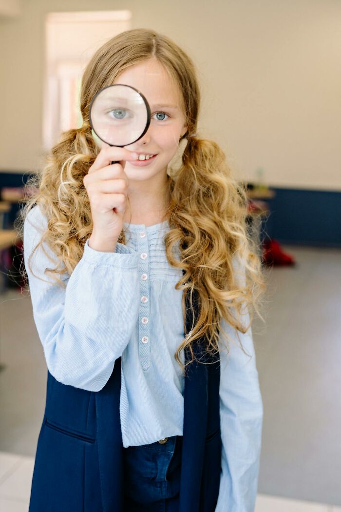 Young girl holding magnifying glass to her eye, representing funny and serious moments of parents raising monsters.