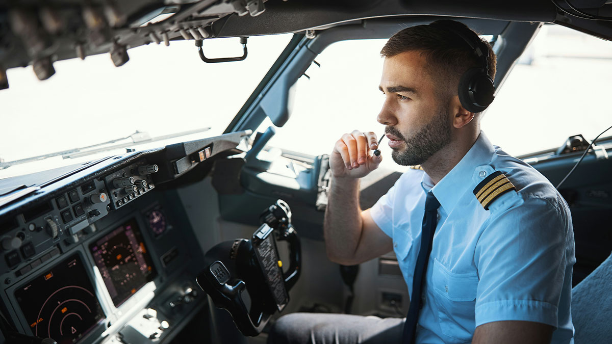 Pilot in cockpit speaking into headset, focused on controls during a mid-flight close call situation.