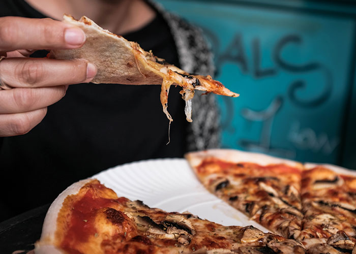 Person holding a slice of pizza with melted cheese, representing restaurant owner and tourists sharing pizzas controversy. Person holding a slice of pizza with melted cheese, representing restaurant owner and tourists sharing pizzas controversy.