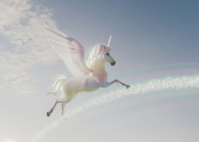 A glowing winged unicorn flying through a bright sky with shimmering sparkles and a pastel rainbow trail.