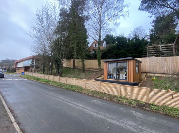 Small wooden structure placed on steep hillside behind a fence, illustrating design and architecture nightmares with poor common sense.