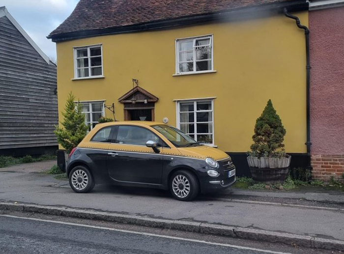 Small car parked on narrow sidewalk next to a house, highlighting design and architecture nightmares in urban planning.