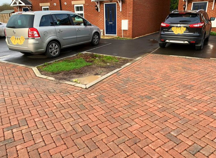 Parking lot with poor design showing a small grass patch disrupting the paved driveway in a design and architecture nightmare.