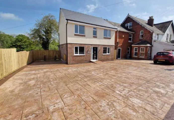 Newly built house with poor design and architecture, featuring a large paved driveway and mismatched adjacent homes.