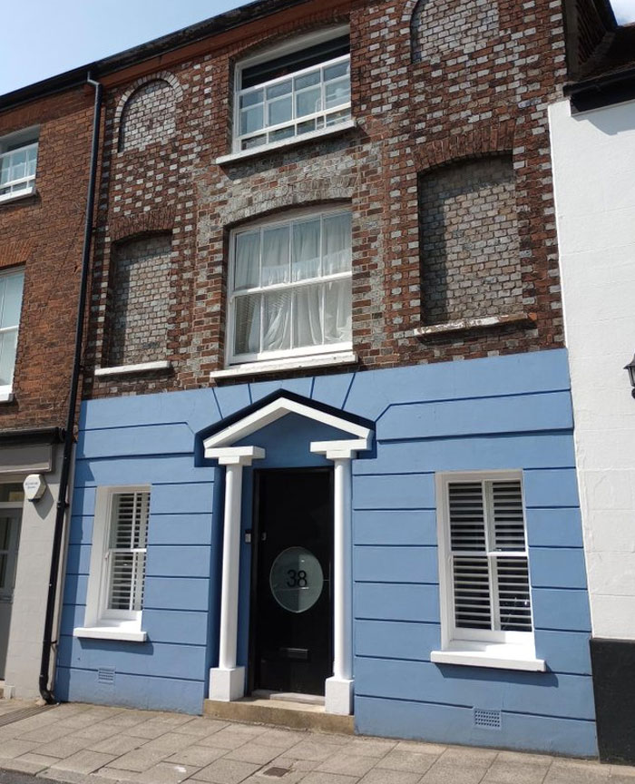 Brick building with bricked-up windows on upper floor and blue painted facade with functional windows on lower floor, architecture nightmare.