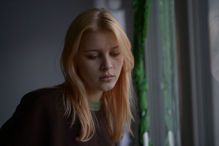 Young woman looking sad and reflective by a window, illustrating emotions related to people who regret having kids.