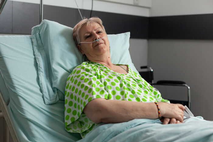 Elderly woman in hospital gown resting in bed with oxygen tube, related to creepy medical cases doctors recall.