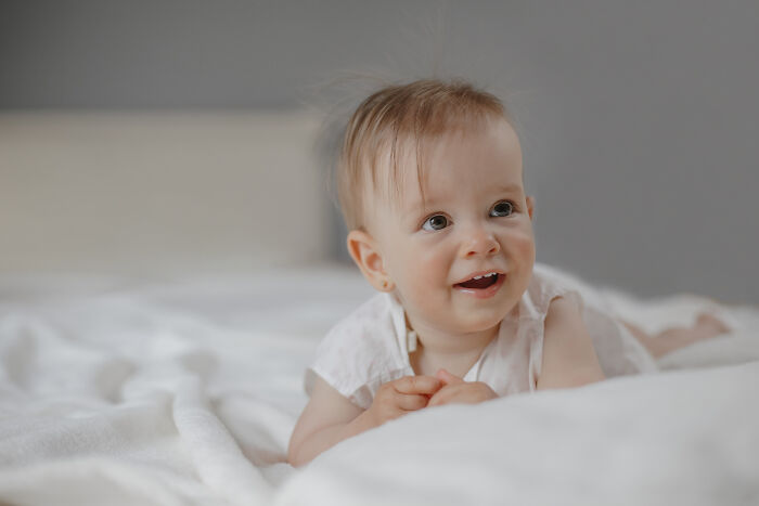 Smiling baby lying on a white bed, illustrating the complex emotions behind people who regret having kids.