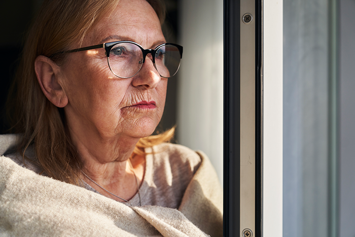 Older woman wearing glasses looking out window with a pouty expression, reflecting a Thanksgiving family conflict.