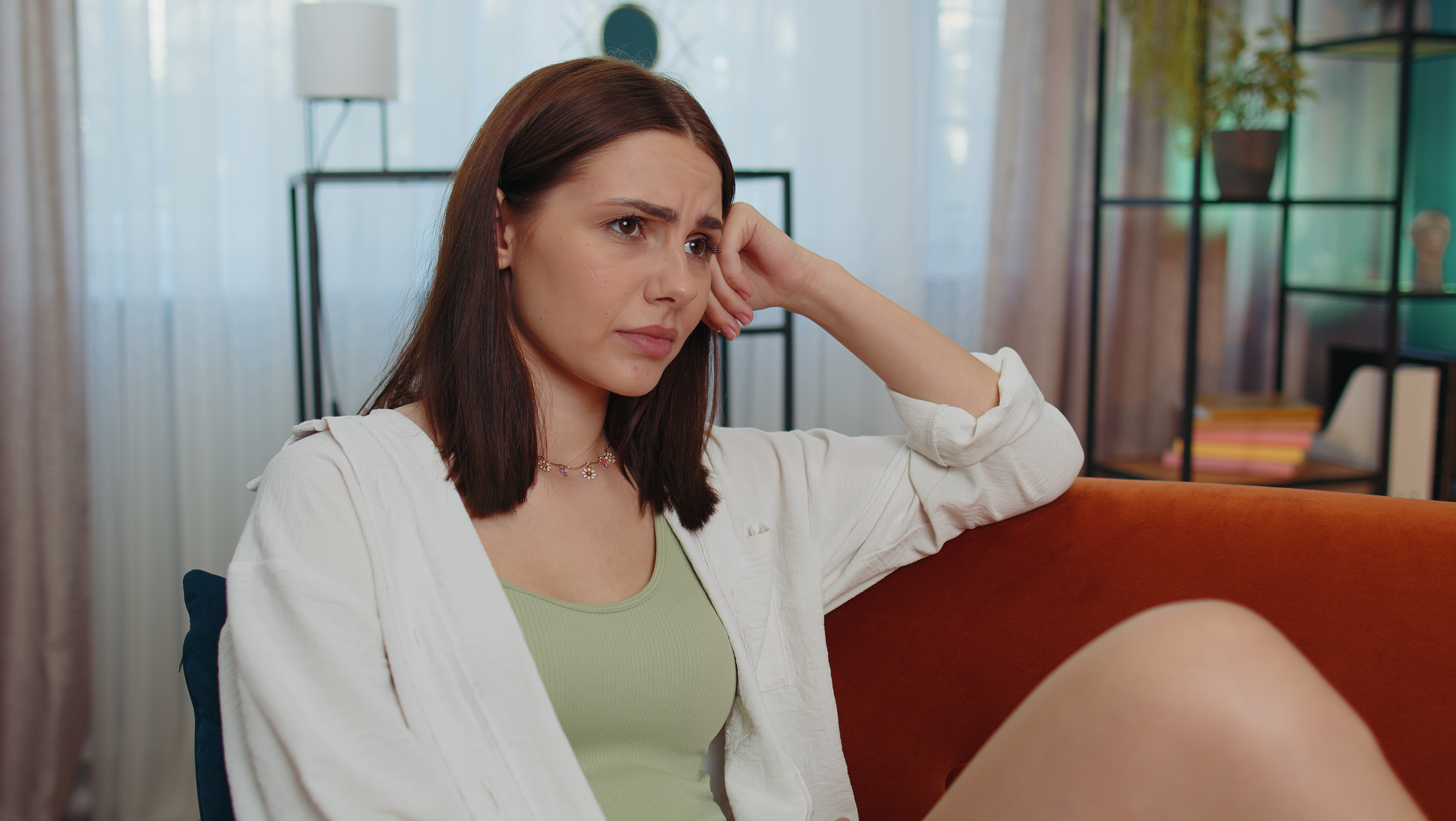 Woman looking frustrated sitting on a couch, reflecting on man inviting guests over and expecting wife to cook.