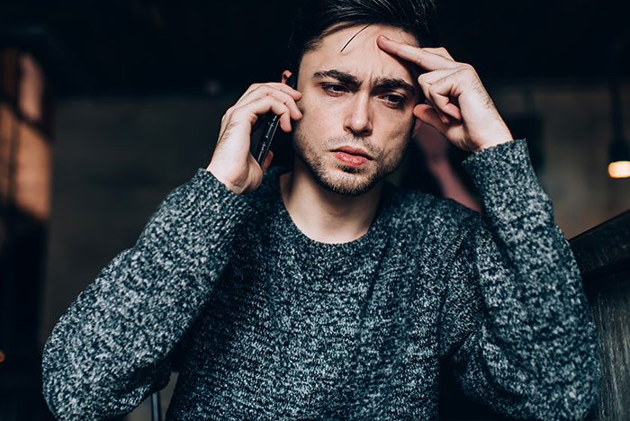 Young man in a gray sweater looking worried while on the phone, reflecting stress over pregnant girlfriend refusing to move together.