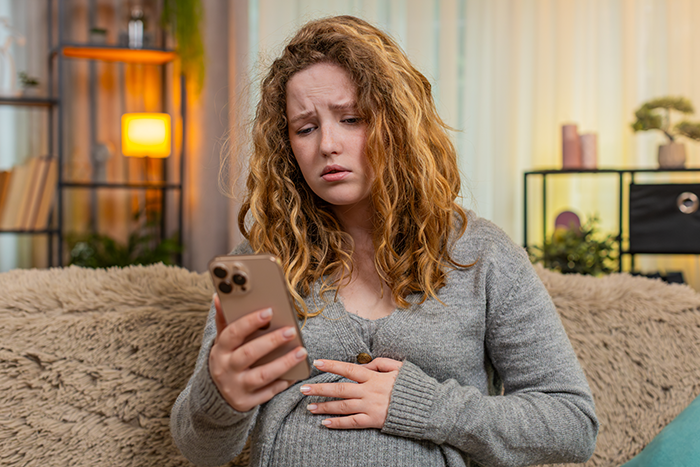 Pregnant woman looking upset while holding phone, illustrating cousin's family accusing her of stealing spotlight. Pregnant woman looking upset while holding phone, illustrating cousin's family accusing her of stealing spotlight.