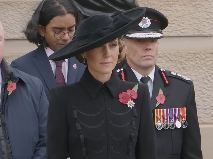 Princess Kate attending a formal event wearing a black hat and coat, with officials in uniform nearby. Princess Kate attending a formal event wearing a black hat and coat, with officials in uniform nearby.