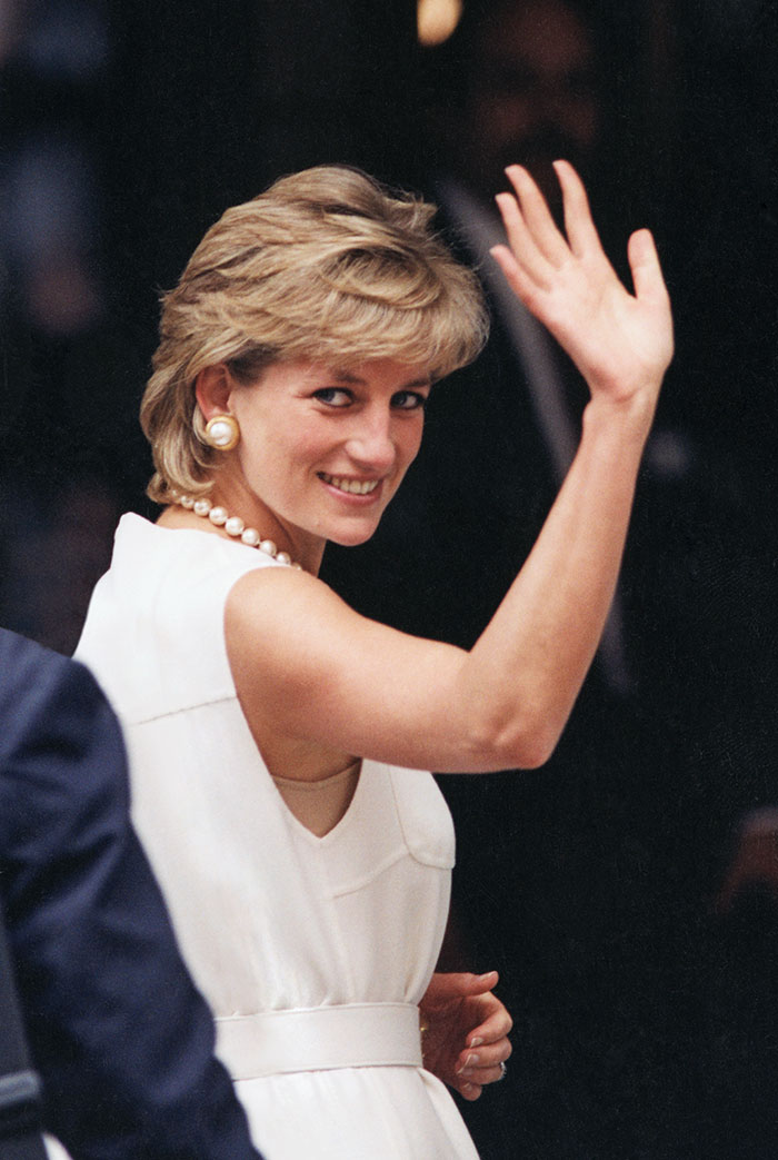 Princess Diana smiling and waving, wearing a white dress with pearl earrings and necklace in a candid moment. Princess Diana smiling and waving, wearing a white dress with pearl earrings and necklace in a candid moment.
