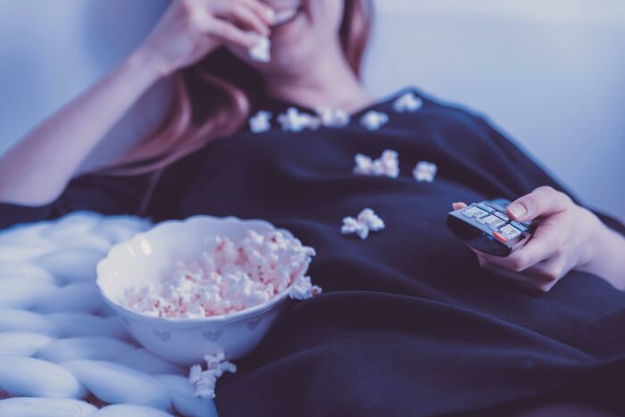 Woman enjoying relaxed moment with popcorn and remote control, illustrating relationship gestures and princess treatment concepts.