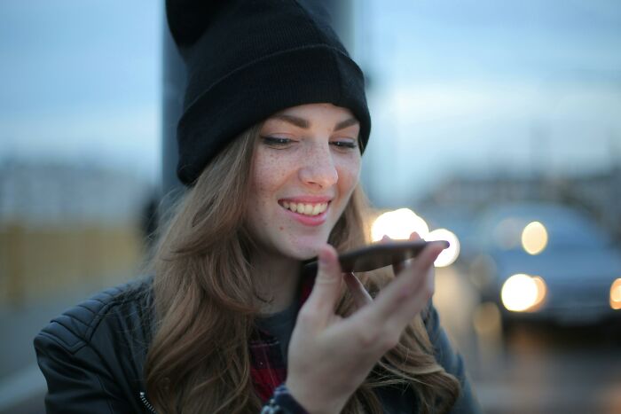 Young woman smiling and speaking on a smartphone outdoors, illustrating relationship gestures and princess treatment discussion.