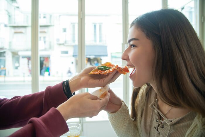 Couple sharing a slice of pizza indoors, showing one of the 30 relationship gestures in a loving moment.