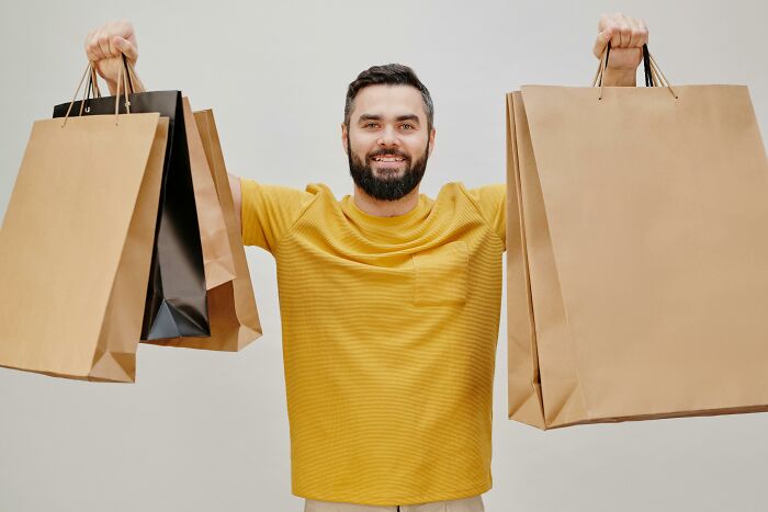 Man smiling and holding multiple shopping bags, illustrating relationship gestures and princess treatment concepts.