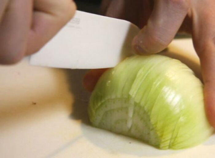 Hands of a pro chef slicing an onion on a cutting board, demonstrating common cooking mistakes amateurs make.